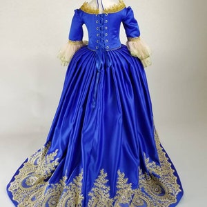 K&ouml;nnte beinhalten: Ein k&ouml;niglich blaues Satin-Ballkleid mit goldener Spitzenverzierung und einem Schn&uuml;rr&uuml;cken. Das Kleid hat einen vollen Rock und ein tailliertes Oberteil.