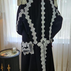 May include: A black velvet coat with white lace trim and epaulettes. The coat features intricate white lace detailing down the back and around the edges, with decorative buttons and a high collar. The coat is a formal garment.