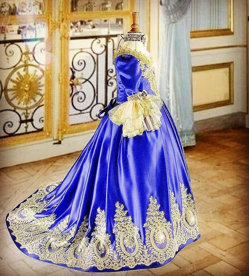 K&ouml;nnte beinhalten: Ein k&ouml;niglich blaues Satin-Ballkleid mit goldener Spitzenverzierung und einem R&uuml;schen&auml;rmel. Das Kleid hat ein tailliertes Oberteil und einen vollen Rock.