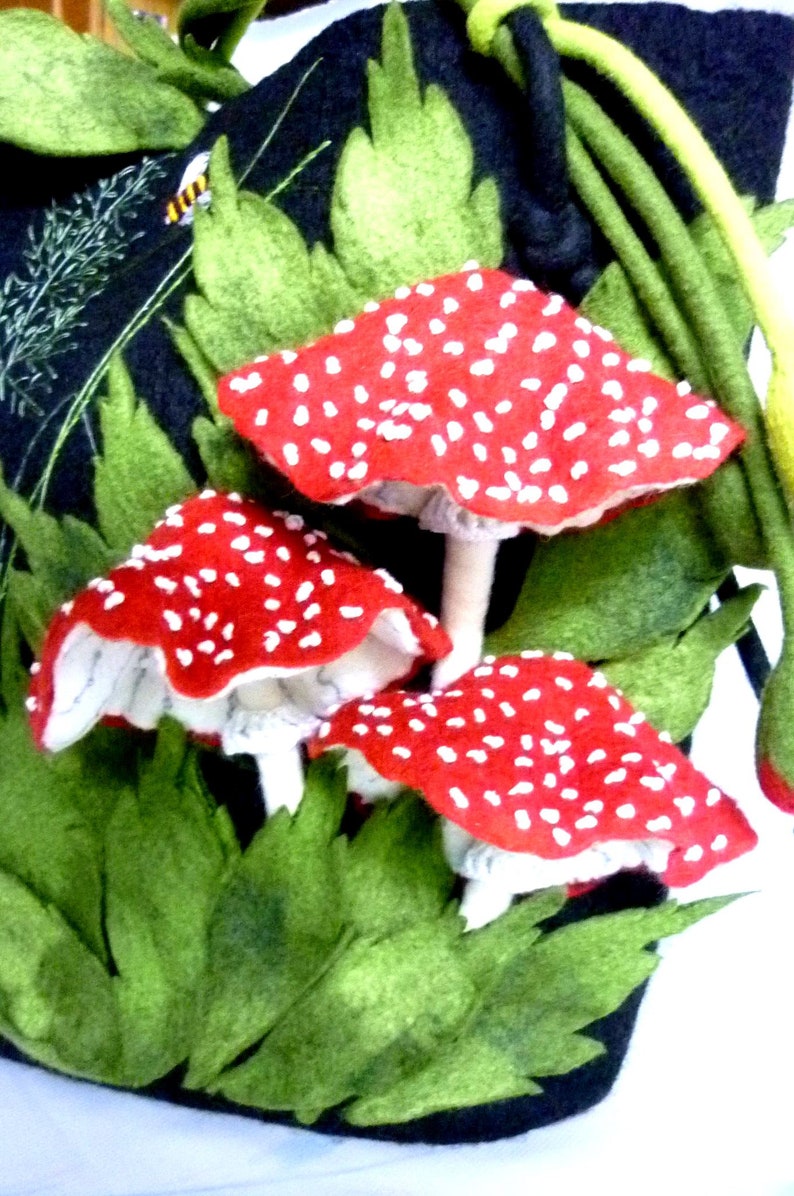 May include: A black felt bag with a green felt handle and three red and white felt mushrooms attached to the front.
