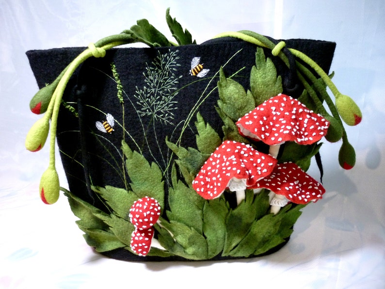May include: A black felt tote bag with a whimsical design featuring red and white mushrooms, green leaves, and yellow bees embroidered on the front.
