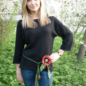 May include: A woman wearing a black sweater and blue jeans with a felt poppy flower belt.