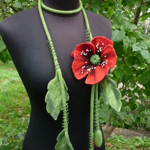 May include: A red felt poppy flower with white accents and green felt leaves hangs from a green felt cord with metal wire accents. The necklace is displayed on a black mannequin.