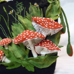 May include: A black felt bag with a drawstring closure, featuring embroidered red and white mushrooms with white lace accents and green leaves. Two yellow bees are embroidered on the bag.