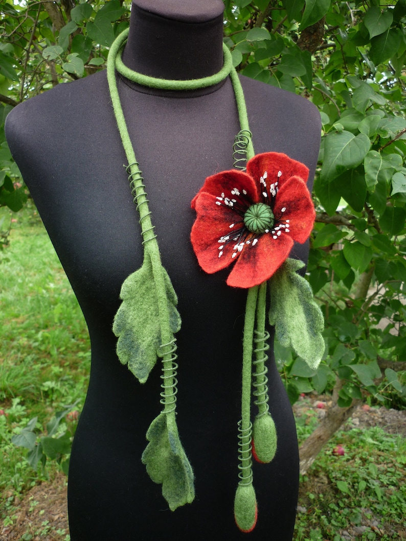 May include: A green felt necklace with a red felt poppy flower and green felt leaves. The necklace is on a black mannequin.