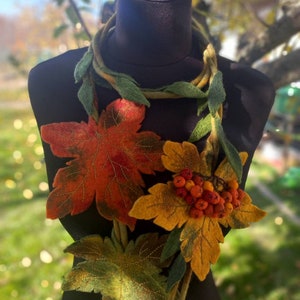 Puede incluir: Un collar de fieltro con hojas de oto&ntilde;o y bayas. El collar presenta una gran hoja de arce naranja y roja, una hoja amarilla con bayas naranjas y hojas verdes m&aacute;s peque&ntilde;as.