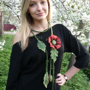 May include: A black sweater with a felt poppy flower necklace. The necklace has green leaves and red poppy flowers.