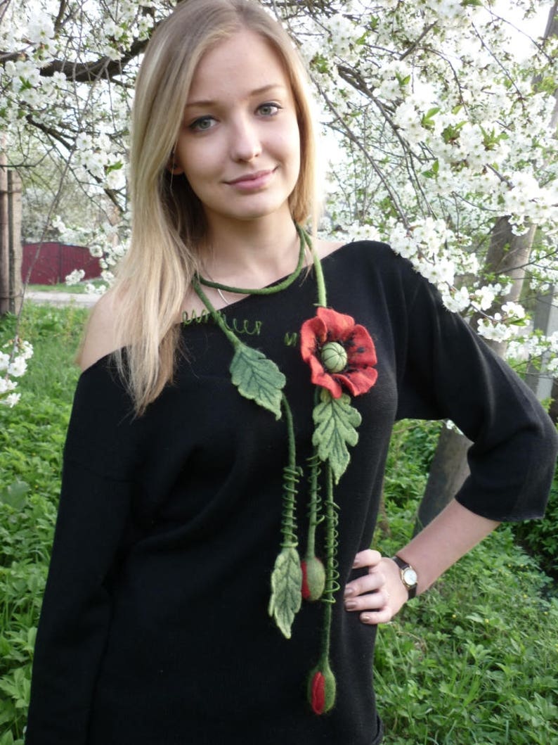 May include: A black sweater with a felt poppy flower necklace. The necklace has green leaves and red poppy flowers.