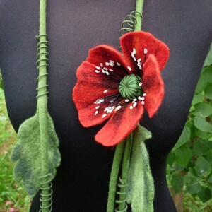 May include: A felt necklace with a red poppy flower and green leaves. The necklace is made of felt and wire.