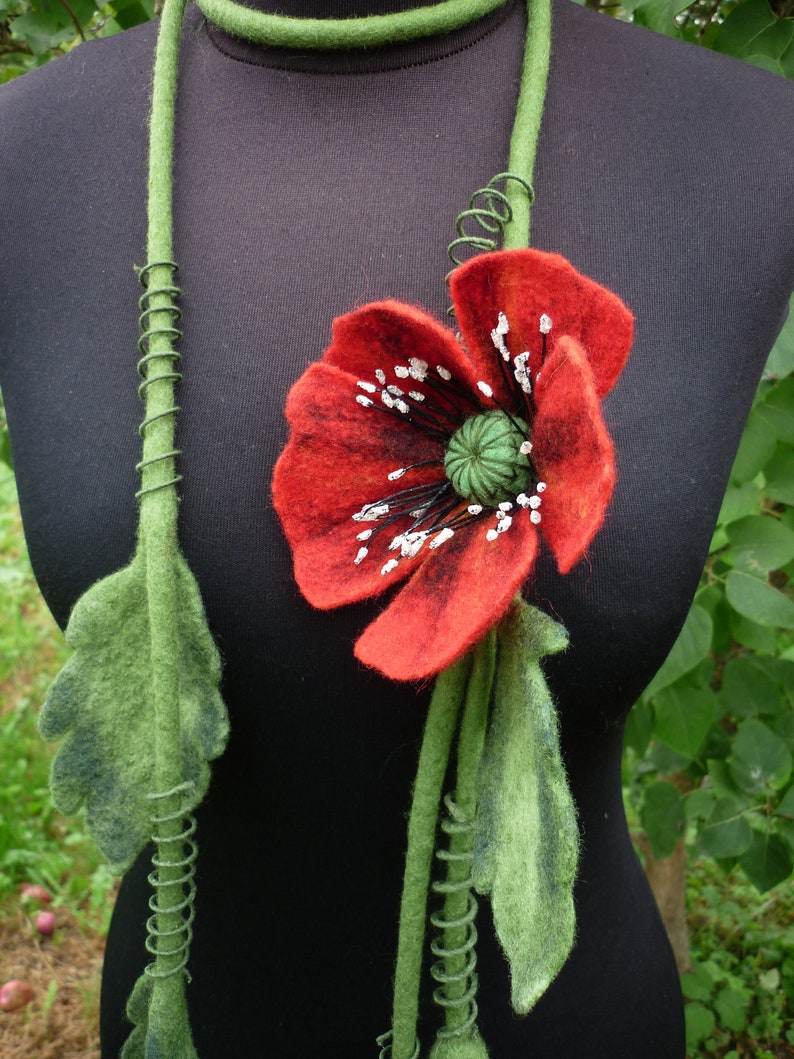 May include: A felt necklace with a red poppy flower and green leaves. The necklace is made of felt and wire.
