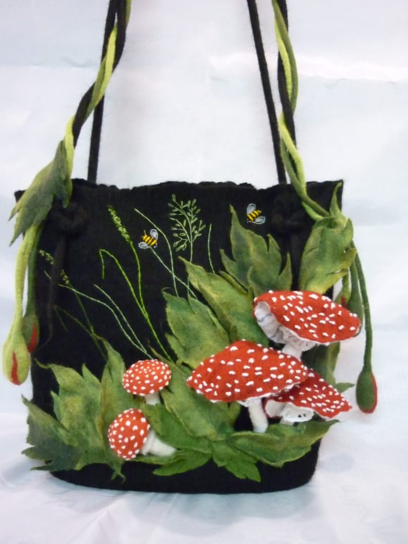 May include: A black felt tote bag with a drawstring closure. The bag is decorated with green felt leaves, red and white felt mushrooms, and embroidered bees and grass.