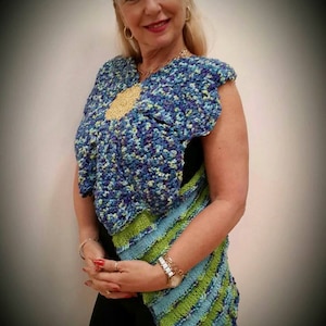 Może przedstawiać: Niebiesko-zielony, szydełkowy bezrękawnik z dużym wzorem kwiatu i złotym guzikiem.