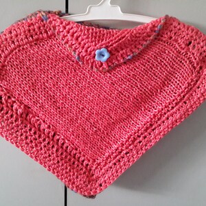 May include: A pink knitted poncho with a blue button and a crocheted trim.