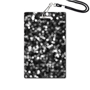 Puede incluir: Tarjeta de identificaci&oacute;n en blanco y negro con un clip plateado y un cord&oacute;n negro. La tarjeta tiene un dise&ntilde;o de c&iacute;rculos blancos sobre un fondo negro.
