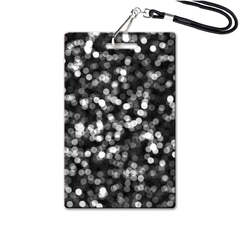 Puede incluir: Tarjeta de identificaci&oacute;n en blanco y negro con un clip plateado y un cord&oacute;n negro. La tarjeta tiene un dise&ntilde;o de c&iacute;rculos blancos sobre un fondo negro.