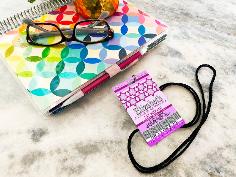 May include: Purple and silver Bat Mitzvah invitation with a ticket design. The invitation reads "Elizabeth is called to the Torah as a Bat Mitzvah".