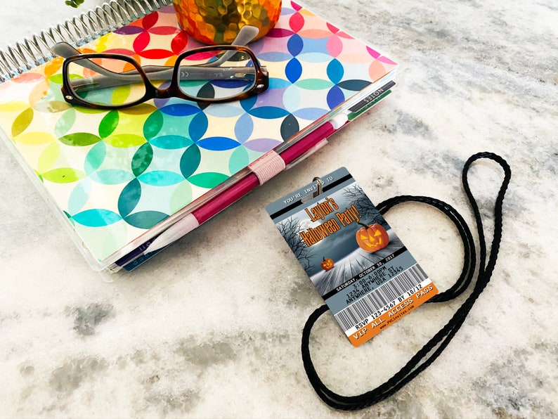 May include: A black lanyard with a Halloween party invitation attached. The invitation is a ticket-style card with a spooky forest scene and a pumpkin. The text on the card reads "Layton's Halloween Party" and includes the date, time, and RSVP information.