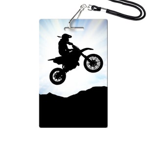 May include: Silhouette of a person riding a dirt bike in mid-air against a blue sky with clouds. The bike is black and the rider is wearing a helmet. The background is a dark hill.