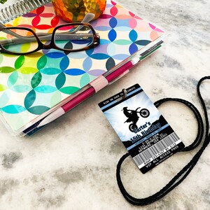 May include: A blue and white birthday party invitation with a black lanyard. The invitation features a silhouette of a motocross rider and the text "Carter's 15th Birthday".