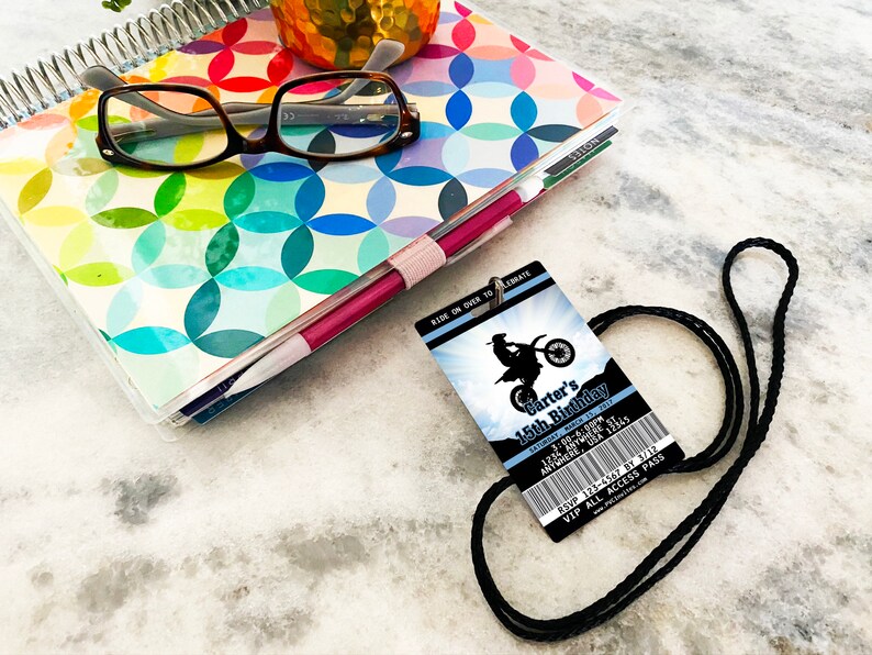 May include: A blue and white birthday party invitation with a black lanyard. The invitation features a silhouette of a motocross rider and the text "Carter's 15th Birthday".