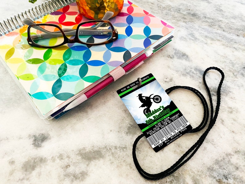 May include: A black lanyard with a green and black birthday party invitation attached. The invitation features a silhouette of a motocross rider and the text "Maddox's 5th Birthday".