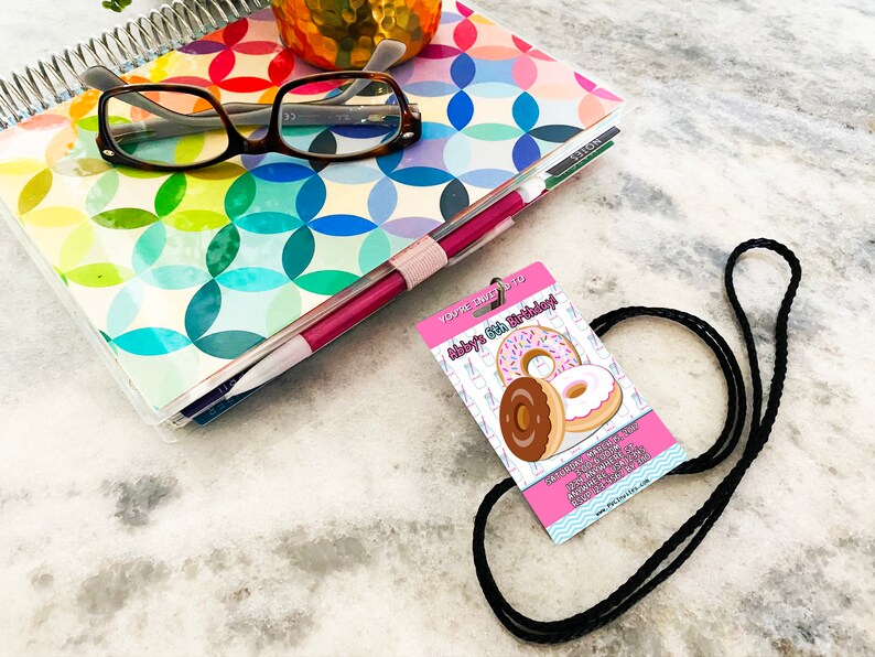 May include: Pink and white birthday party invitation with a black lanyard. The invitation says "You're invited to Abby's 6th Birthday!" and features a graphic of three donuts.