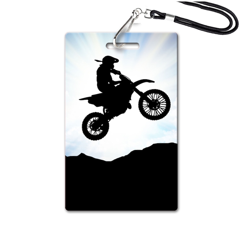May include: Silhouette of a motocross rider jumping over a hill against a blue sky with clouds. The rider is wearing a helmet and goggles. The motorcycle is black and has a white background.