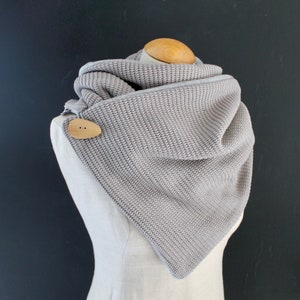 Könnte beinhalten: Ein grauer Strick Schal mit einem Holz Knopf. Der Schal ist gefaltet und auf einer Schaufensterpuppe ausgestellt.