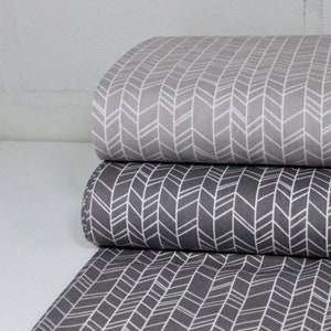 May include: Three rolls of fabric with a white chevron pattern on a grey background. The top roll is a lighter grey, the middle roll is a darker grey, and the bottom roll is a dark grey.