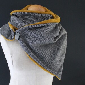 May include: A grey and black herringbone infinity scarf with a mustard yellow fleece lining. The scarf has a button closure.