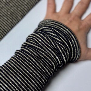 Puede incluir: Calentadores de brazo a rayas negras y doradas. Los calentadores est&aacute;n hechos de un tejido el&aacute;stico y tienen un brillo sutil.
