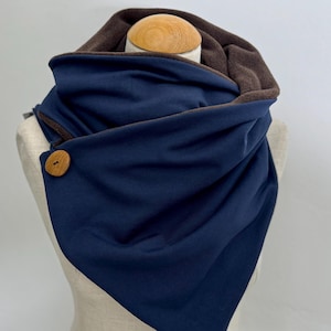May include: A navy blue infinity scarf with a brown fleece lining and a wooden button. The scarf is folded in a triangular shape and is displayed on a mannequin.