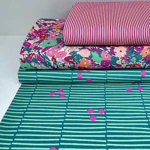 Könnte beinhalten: Drei Stoffmuster, die übereinander gestapelt sind. Das oberste Muster ist pink und weiß gestreift, das mittlere Muster ist ein Blumendruck mit pinken, grünen und orangefarbenen Blumen und das unterste Muster ist türkis mit weißen Streifen und pinken Punkten.
