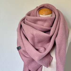 Könnte beinhalten: Staubrosa Schal, drapiert auf einer Schaufensterpuppe. Der Schal besteht aus einem weichen, strukturierten Stoff und ist in einem Wickeldesign gehalten. Ein kleines, dunkelgraues quadratisches Etikett ist am Schal befestigt. Das Design des Schals umfasst spitze Enden.