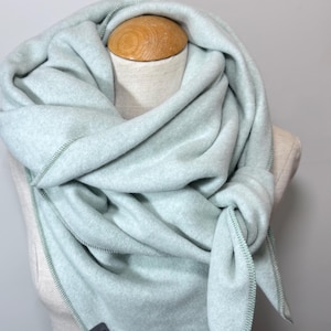 Könnte beinhalten: Hellblauer Fleece-Schal, der um den Hals einer Schaufensterpuppe drapiert ist. Der Schal ist vorne geknotet und hat einen Knopfverschluss. Die Kanten sind mit kontrastierenden grünen Nähten versehen.