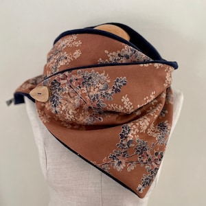 Peut inclure: Une écharpe marron et bleu marine à imprimé floral et un bouton en bois. L'écharpe est pliée et exposée sur un mannequin blanc.