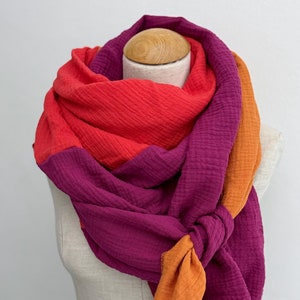 Op de afbeelding: Een veelkleurige sjaal met een verloop van oranje, rood en paars. De sjaal is gemaakt van een zachte, textuurrijke stof en is in een knoop geknoopt.