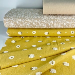 Può includere: Una pila di rotoli di tessuto in vari colori e fantasie. Il rotolo superiore è beige tinta unita, seguito da un tessuto beige con un motivo floreale bianco. Sotto c'è un tessuto giallo senape con un motivo di pecore.