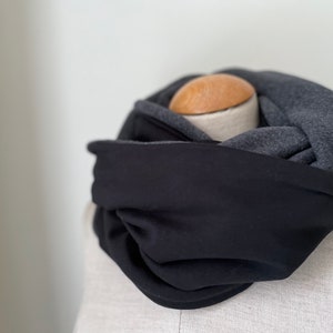 Könnte beinhalten: Ein schwarzer und grauer Loop-Schal auf einer Schaufensterpuppe. Der Schal besteht aus weichem Stoff und scheint eine Mischung aus schwarzen und grauen Materialien zu sein. Der Schal ist kreisförmig gewickelt und zeigt seine Textur und Farbvariationen.