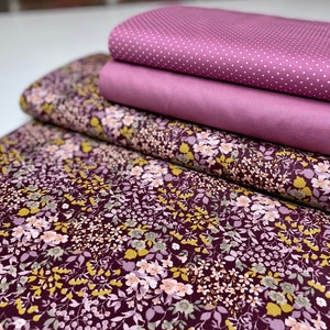 Op de afbeelding: Een stapel van vier stofstalen in tinten roze en paars. De bovenste staal heeft een wit stippenpatroon, de tweede staal is effen roze, de derde staal is effen paars en de onderste staal heeft een bloemenpatroon met roze, paarse en gele bloemen op een donkerpaarse achtergrond.