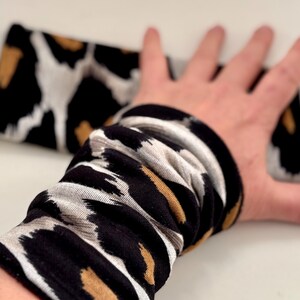 Peut inclure: Un chauffe-bras à motif noir, blanc et or. Le chauffe-bras est fait d'un tissu doux et extensible.