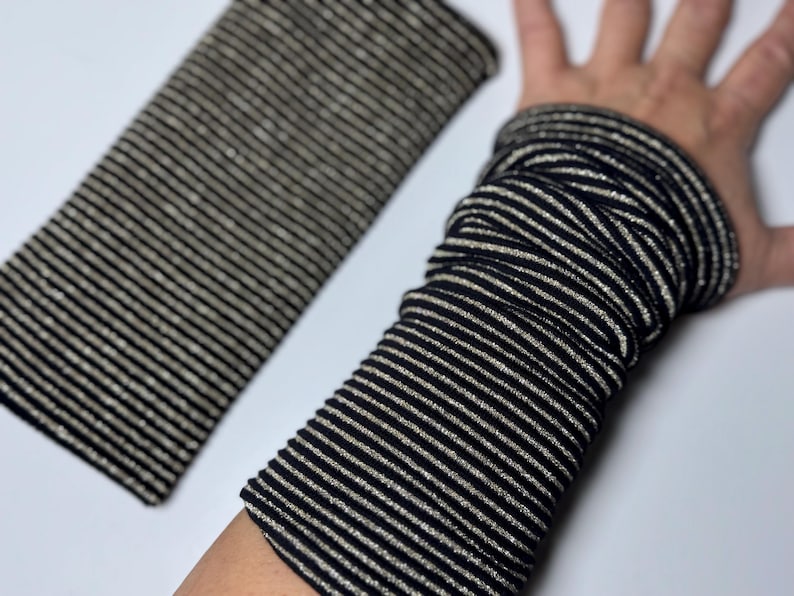 Puede incluir: Calentadores de brazo de tela a rayas negras y plateadas. La tela es el&aacute;stica y tiene un brillo sutil.