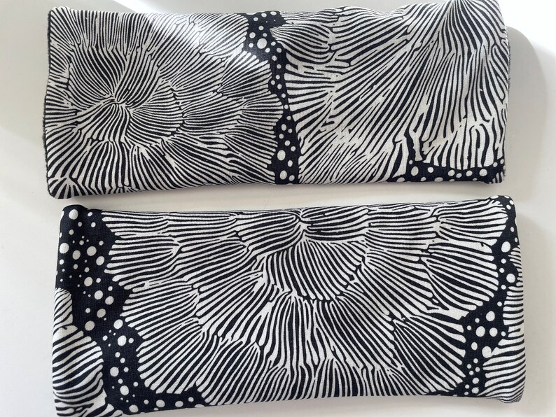 May include: Two black and white eye pillows with a geometric pattern. The pattern is made up of lines and dots.