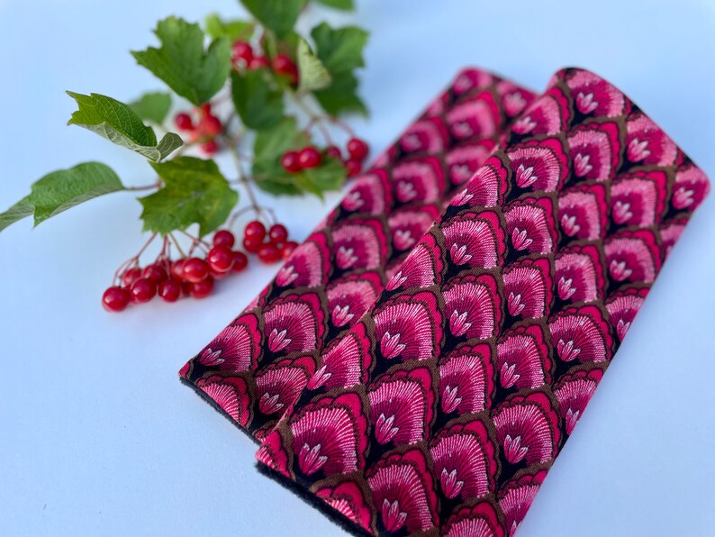 May include: Two pink and black patterned fabric seatbelt covers. The fabric has a repeating pattern of pink flowers with brown accents on a black background.