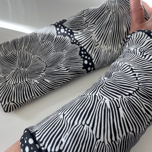 May include: A pair of black and white arm warmers with a wavy, abstract pattern. The pattern resembles a series of concentric circles.