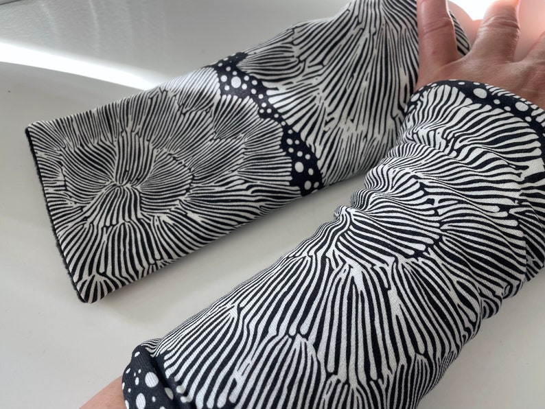 May include: A pair of black and white arm warmers with a wavy, abstract pattern. The pattern resembles a series of concentric circles.