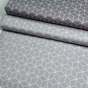 Może przedstawiać: Trzy rolki szarej tkaniny z białym geometrycznym wzorem kostki. Tkanina jest złożona i ułożona w stos, z górną rolką w ciemniejszym odcieniu szarości. Wzór jest spójny na wszystkich warstwach.