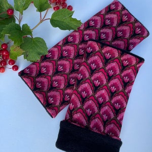 May include: A pair of pink and black arm warmers with a floral pattern. The warmers are made of a soft, comfortable fabric and have a black fleece lining.