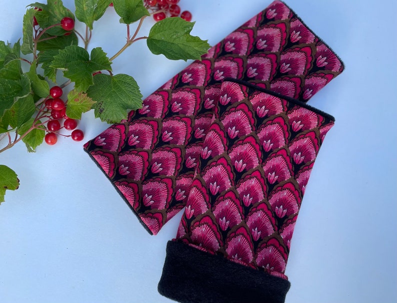 May include: A pair of pink and black arm warmers with a floral pattern. The warmers are made of a soft, comfortable fabric and have a black fleece lining.