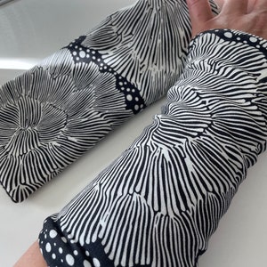 May include: A pair of black and white arm warmers with a swirling, organic pattern. The fabric has a textured, almost woven look.
